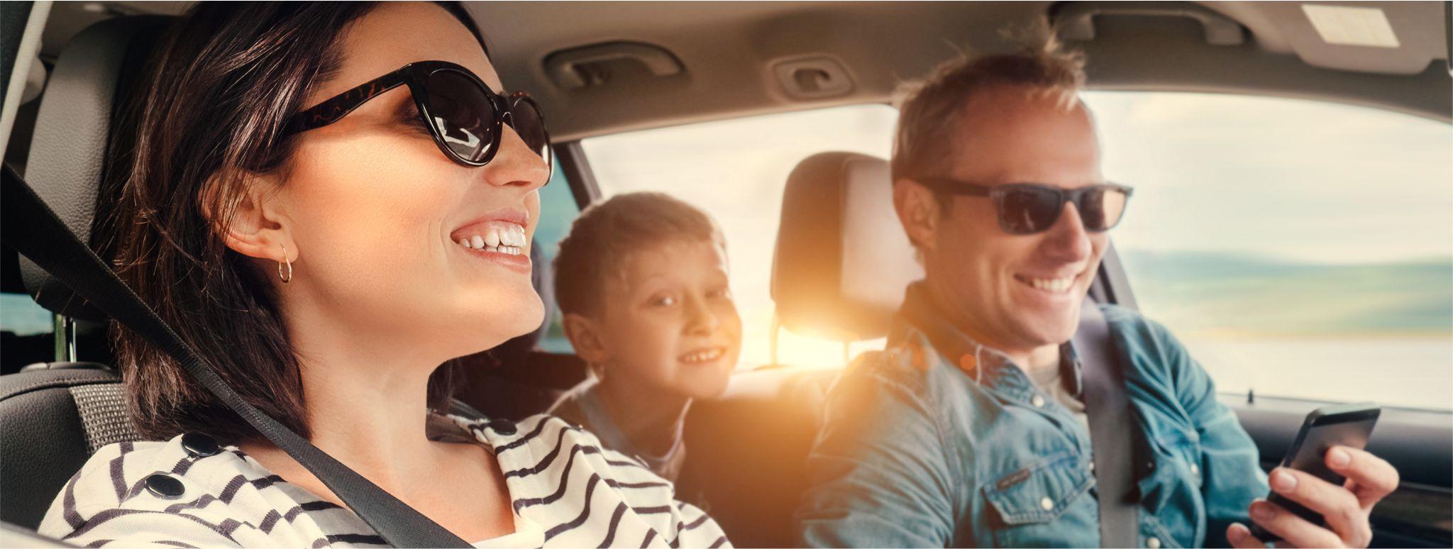 A family driving in a car wearing sunglasses smiling